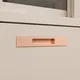 HA 00203 L Ottr Concealed Handle Rose Gold Dual Tone Finish 12in â close-up of rose gold copper handle on cream drawer