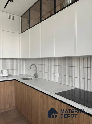Minimalist kitchen with white marble-look countertop, wood laminate base cabinets, and vertical white subway backsplash tiles