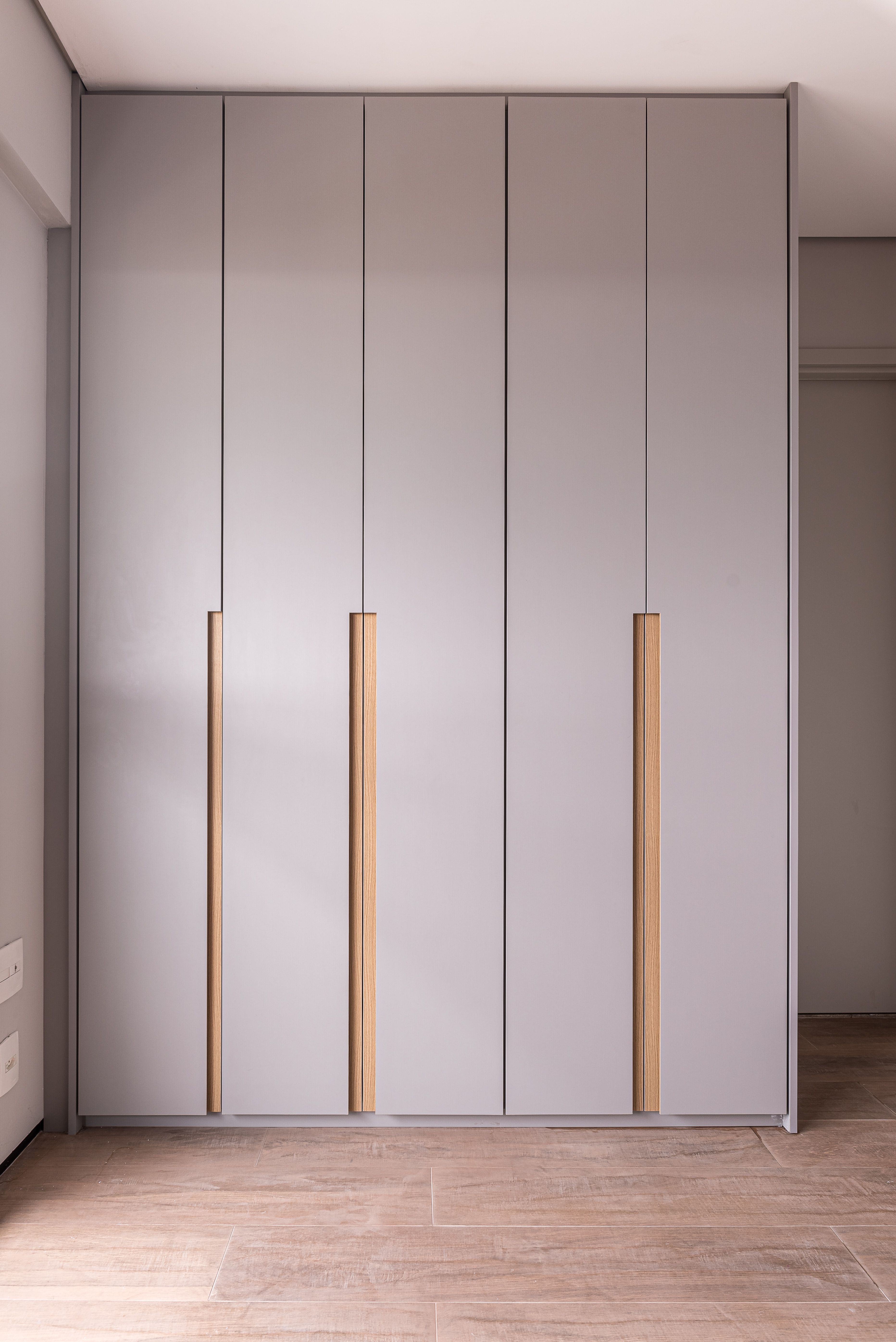 Minimalist wardrobe with matte grey laminate shutters and oak wood handles on wood-look tile flooring | Material Depot