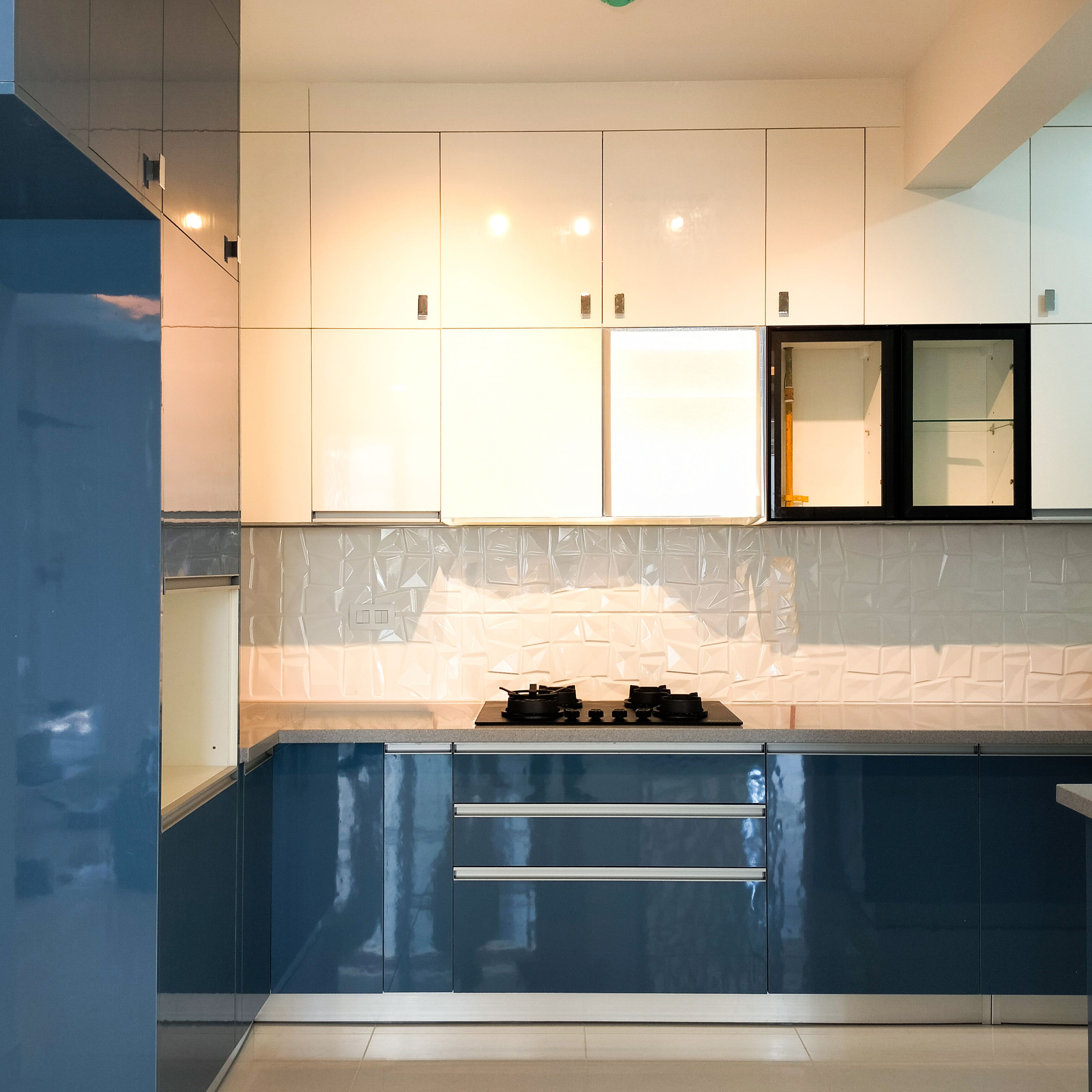 Modern dual tone kitchen with glossy blue and white laminate, geometric white backsplash tile, and quartz countertop in Bengaluru | Material Depot