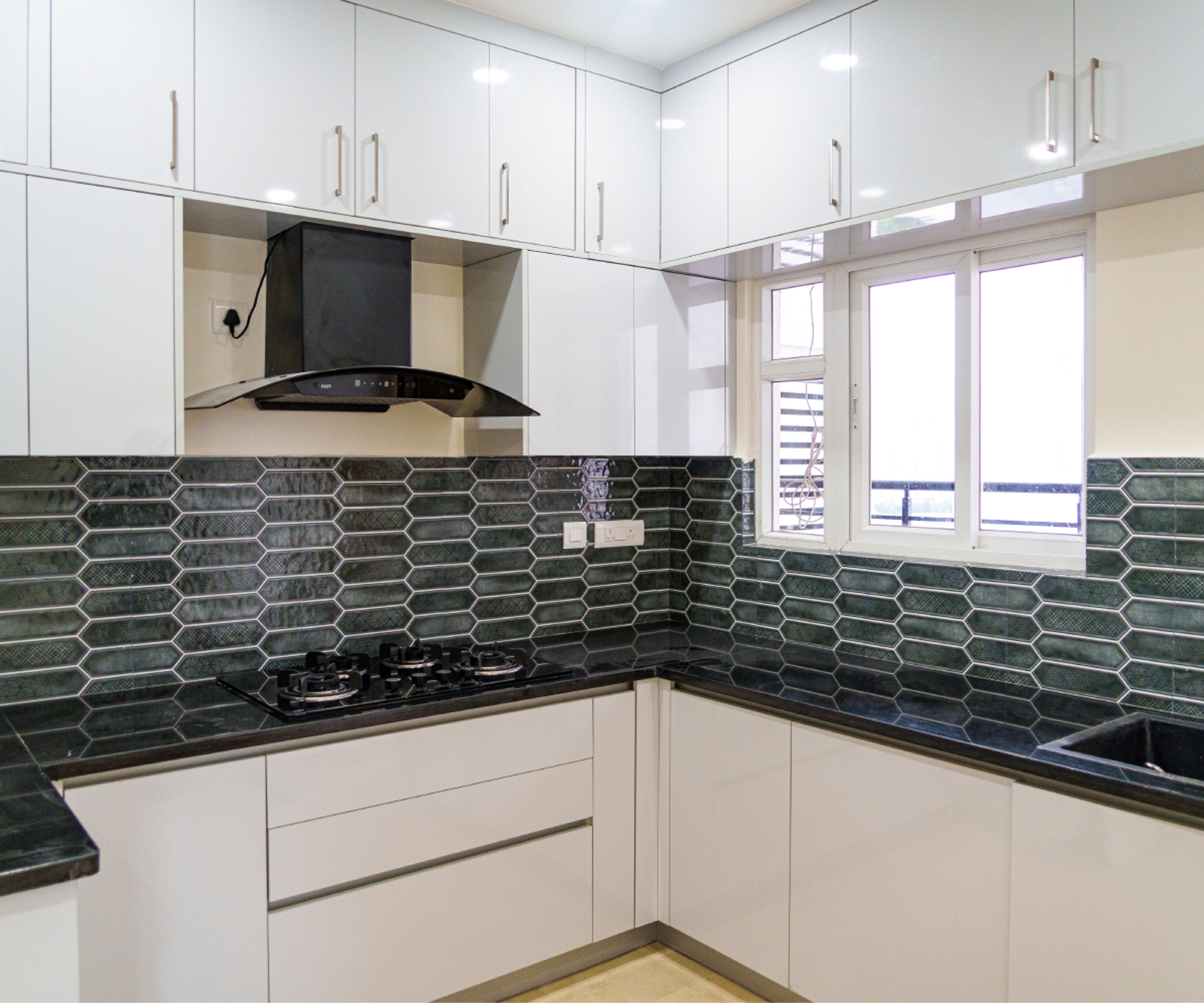 Modern kitchen with glossy white laminate cabinets, black granite countertop, and green geometric backsplash tiles in Bengaluru | Material Depot