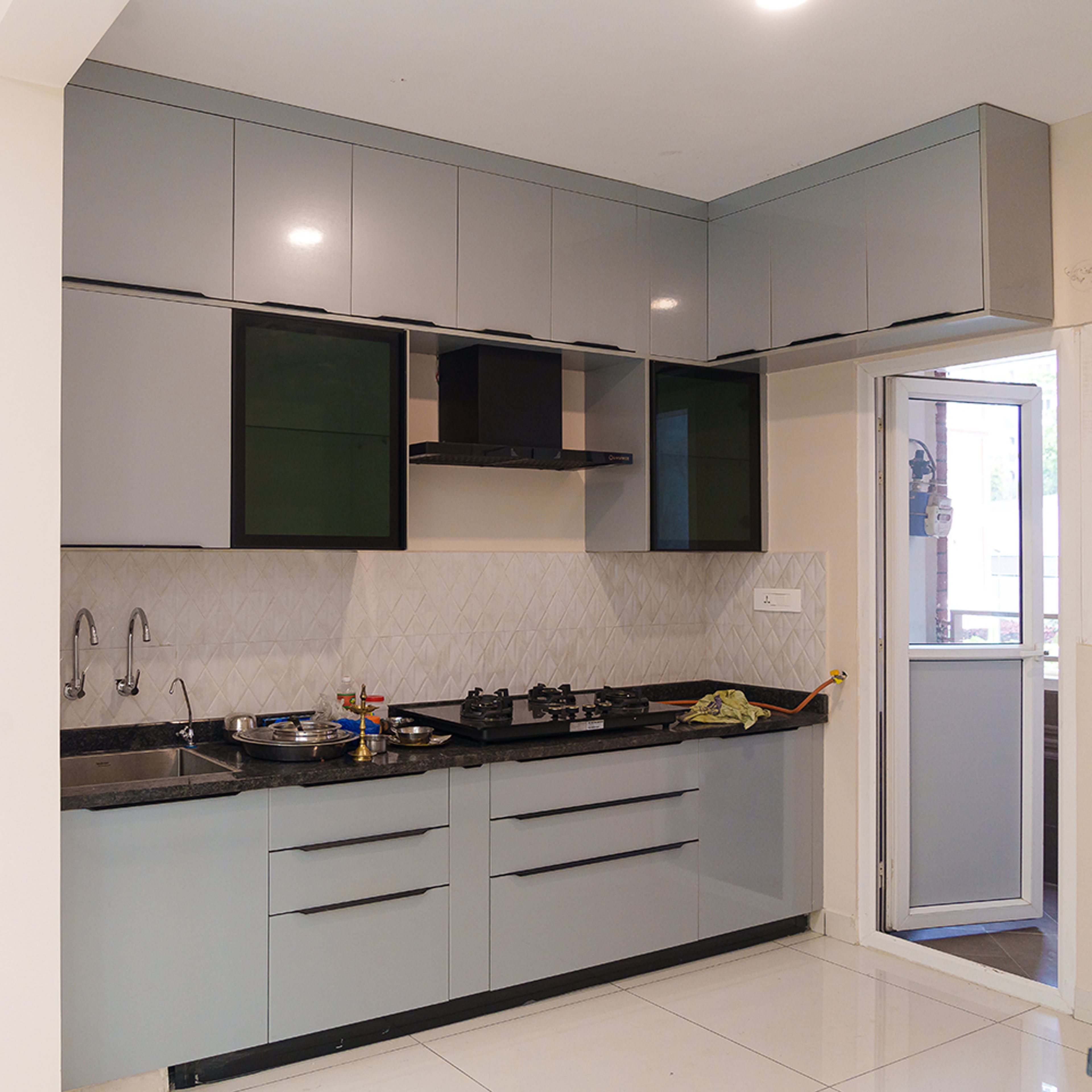 Modern kitchen with grey high gloss laminate cabinets, black granite countertop, and white geometric backsplash tile in Bengaluru | Material Depot