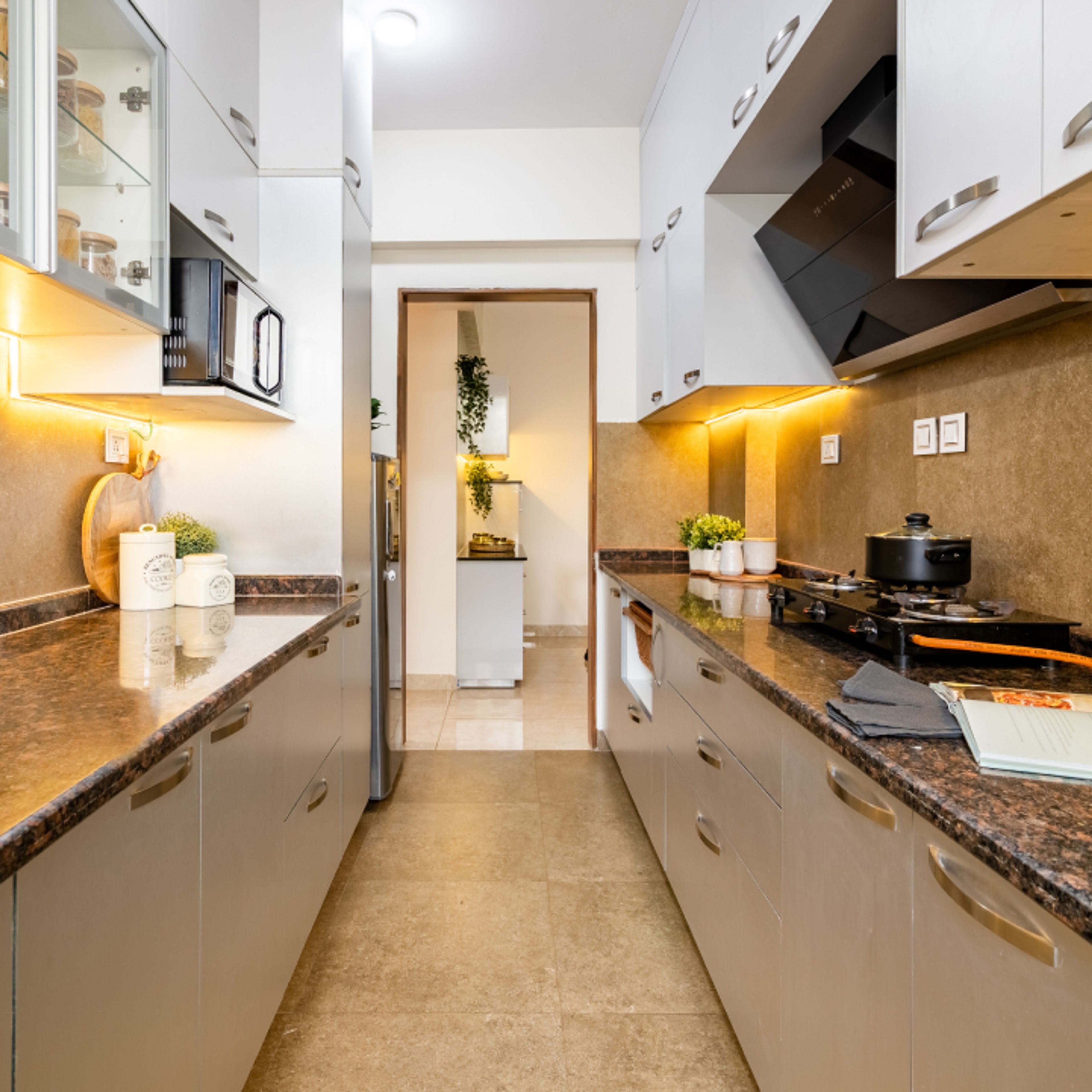 Modern parallel kitchen with frosty white laminate cabinets, brown granite countertop, and beige stone wall tiles in Bengaluru | Material Depot