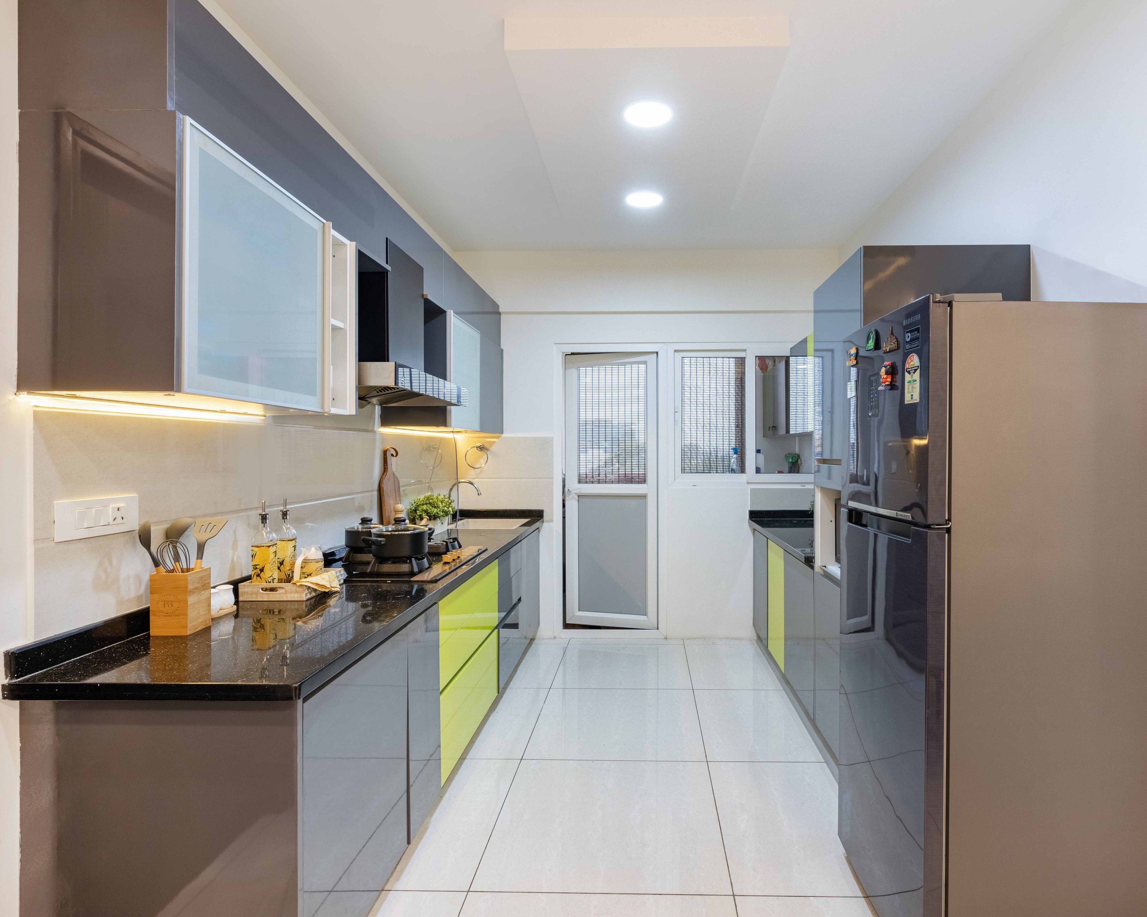 Modern parallel kitchen with grey and lime green high gloss laminate, black granite countertop, and white floor tiles in Bengaluru | Material Depot