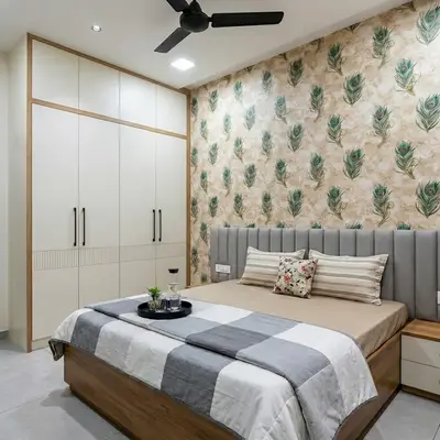 Modern bedroom with peacock feather patterned wallpaper, frosty white laminate wardrobe, and light wood bed